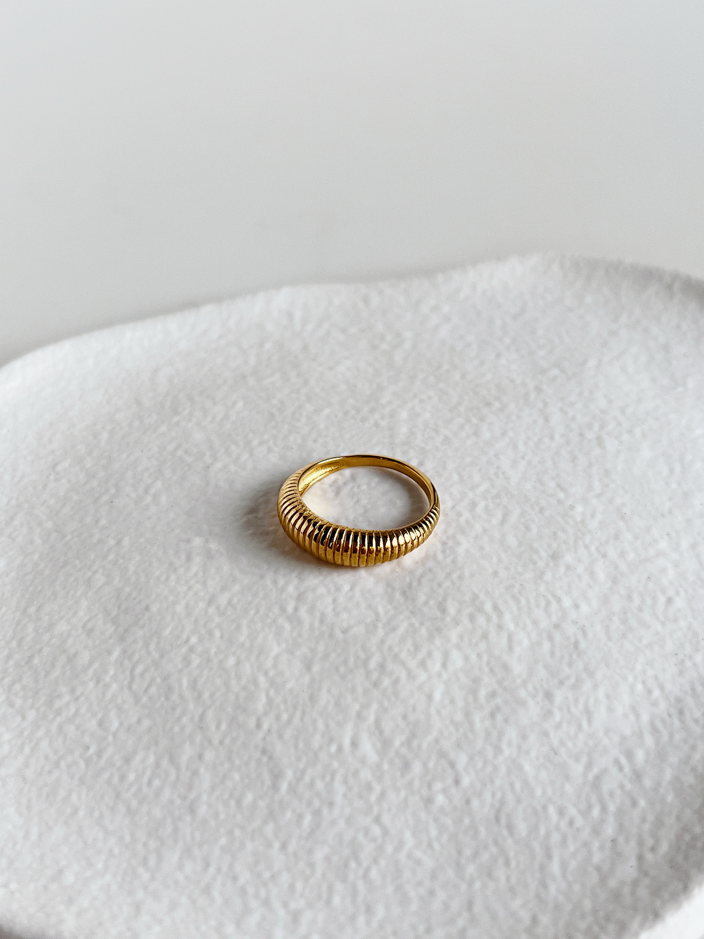 Gold ribbed ring on a textured white surface