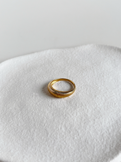 Gold ribbed ring on a textured white surface