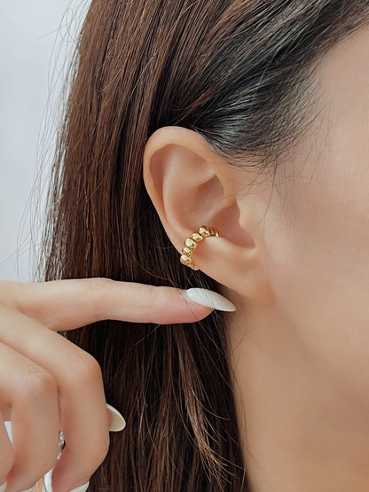 Close-up of an ear wearing a gold beaded ear cuff earring with a blurred background