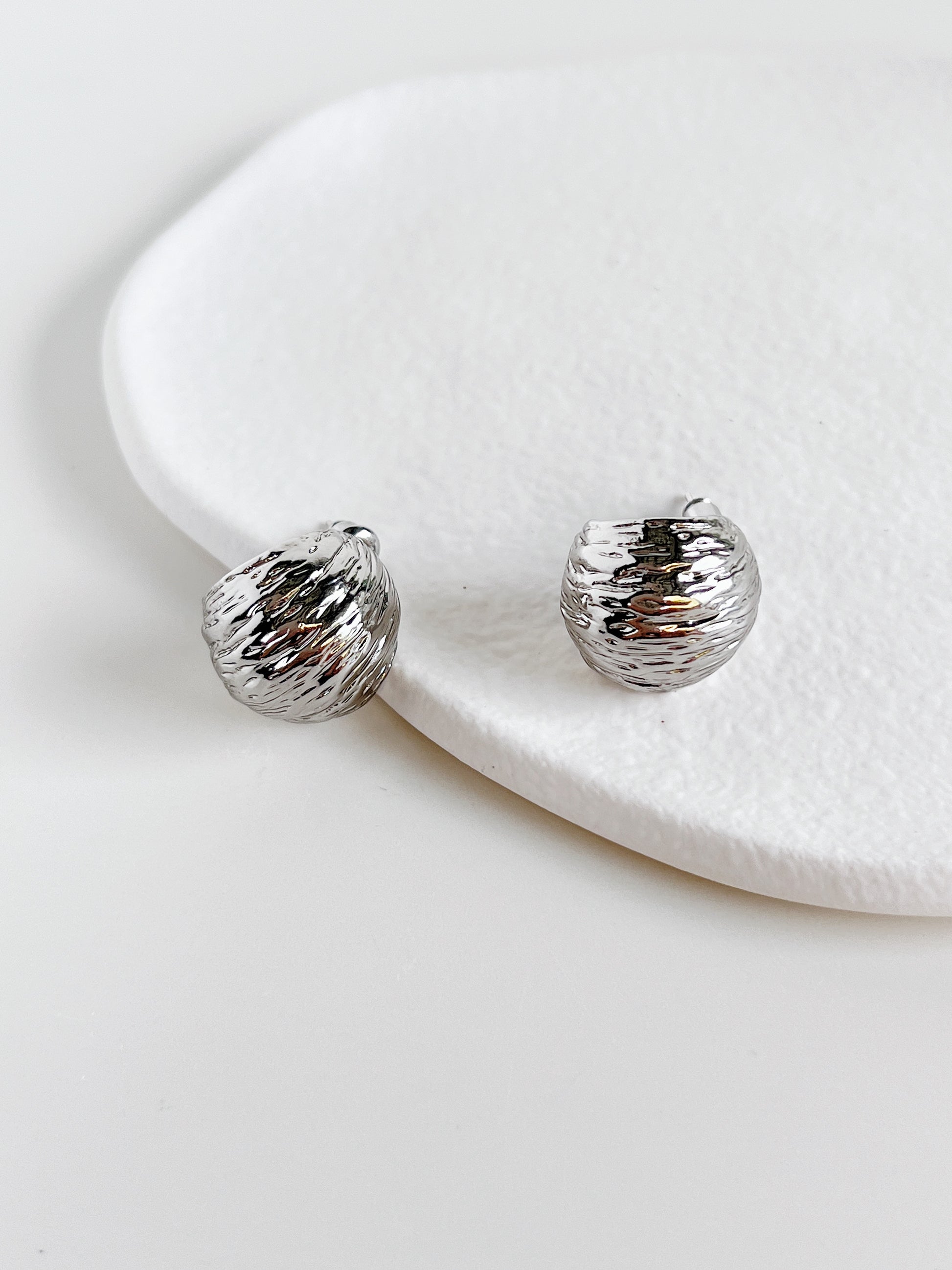 Silver textured earrings on a white ceramic surface