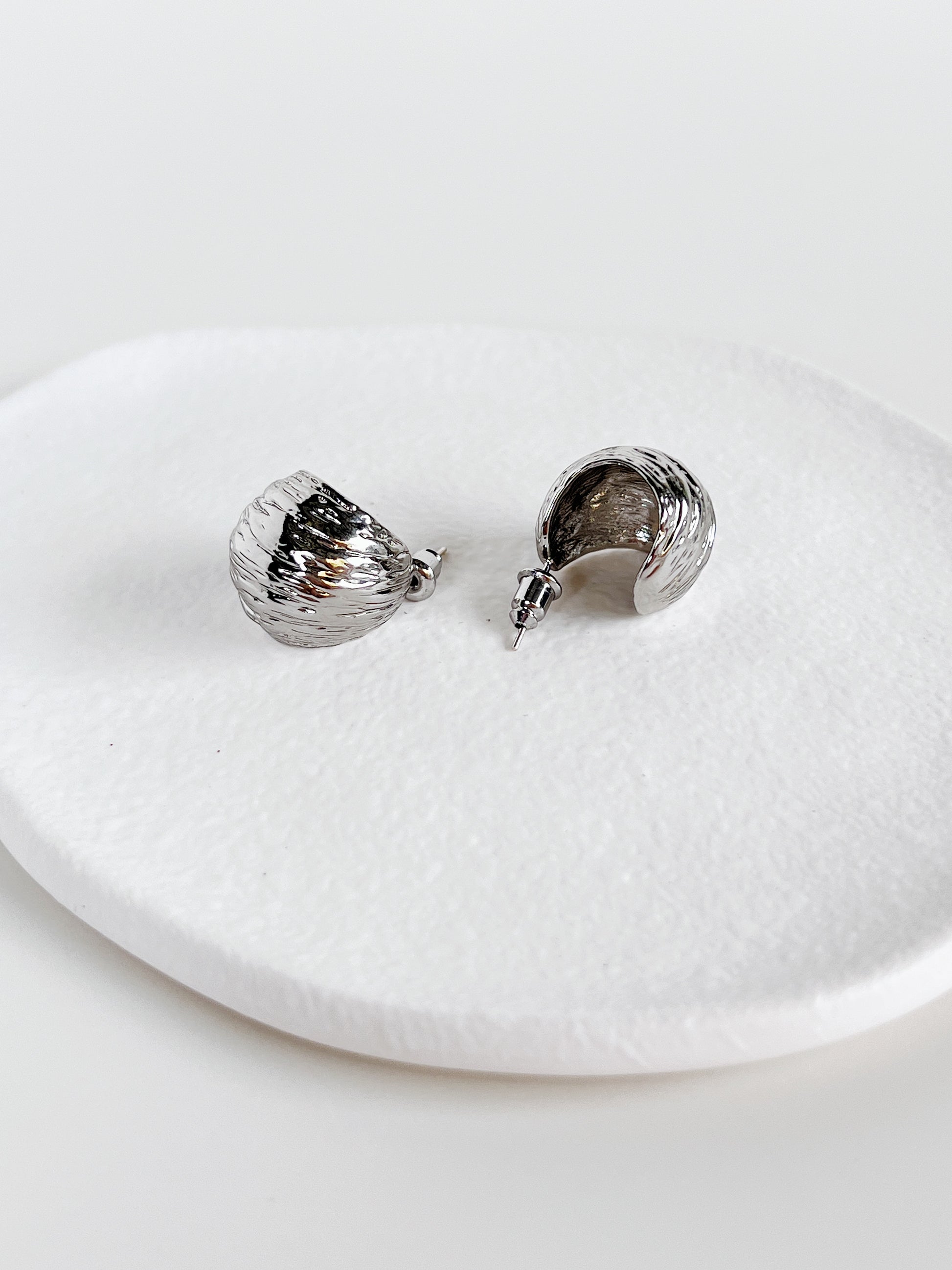 Pair of silver textured hoop earrings on a white plate