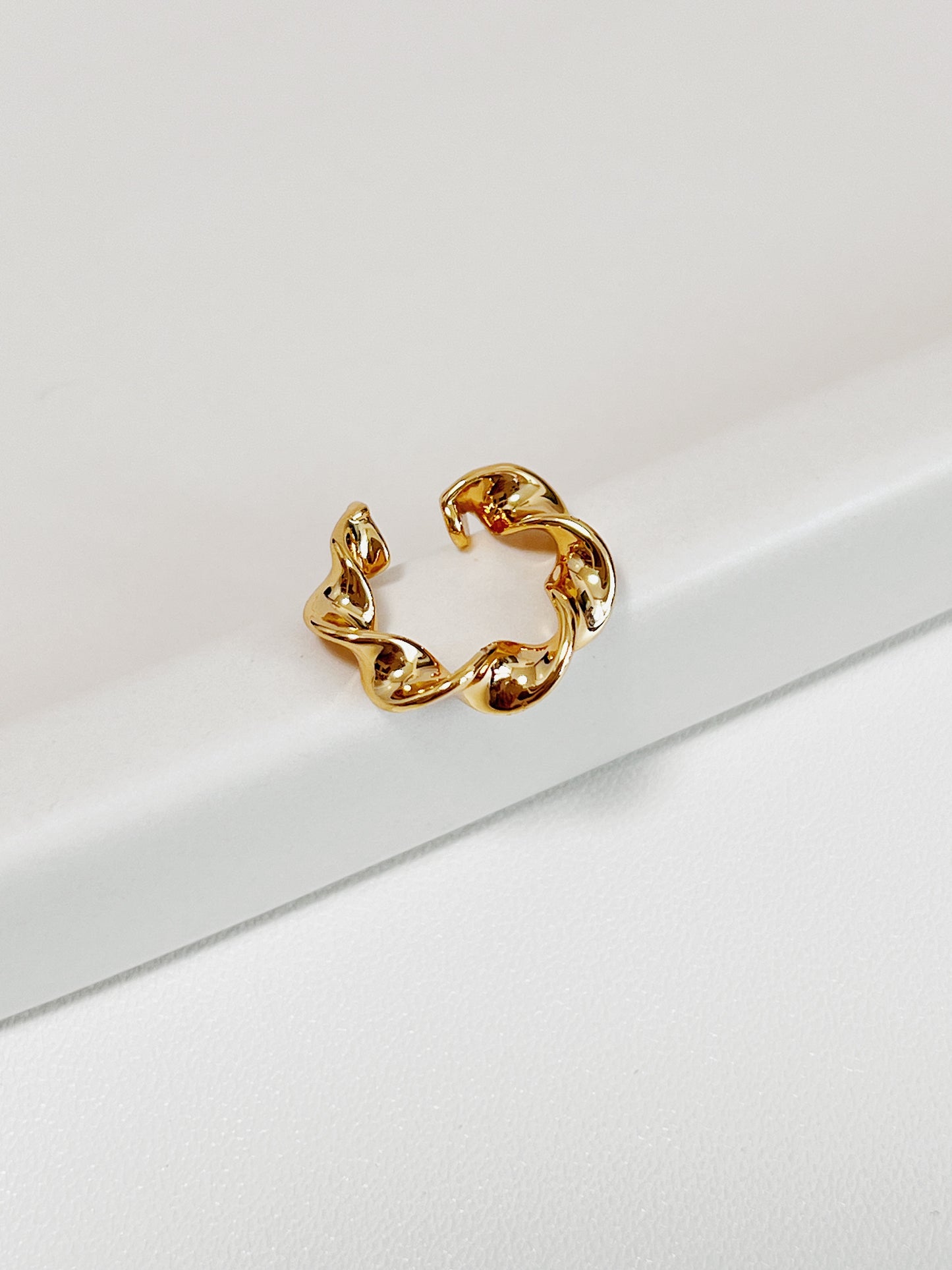 Gold twisted ear cuff earring on a beige background