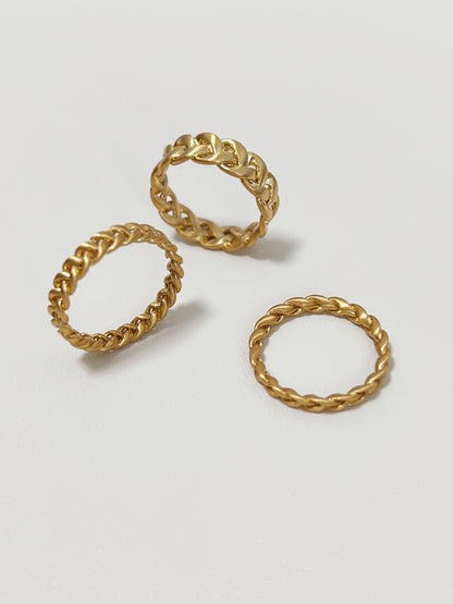 Three gold chain-style rings on a light gray background