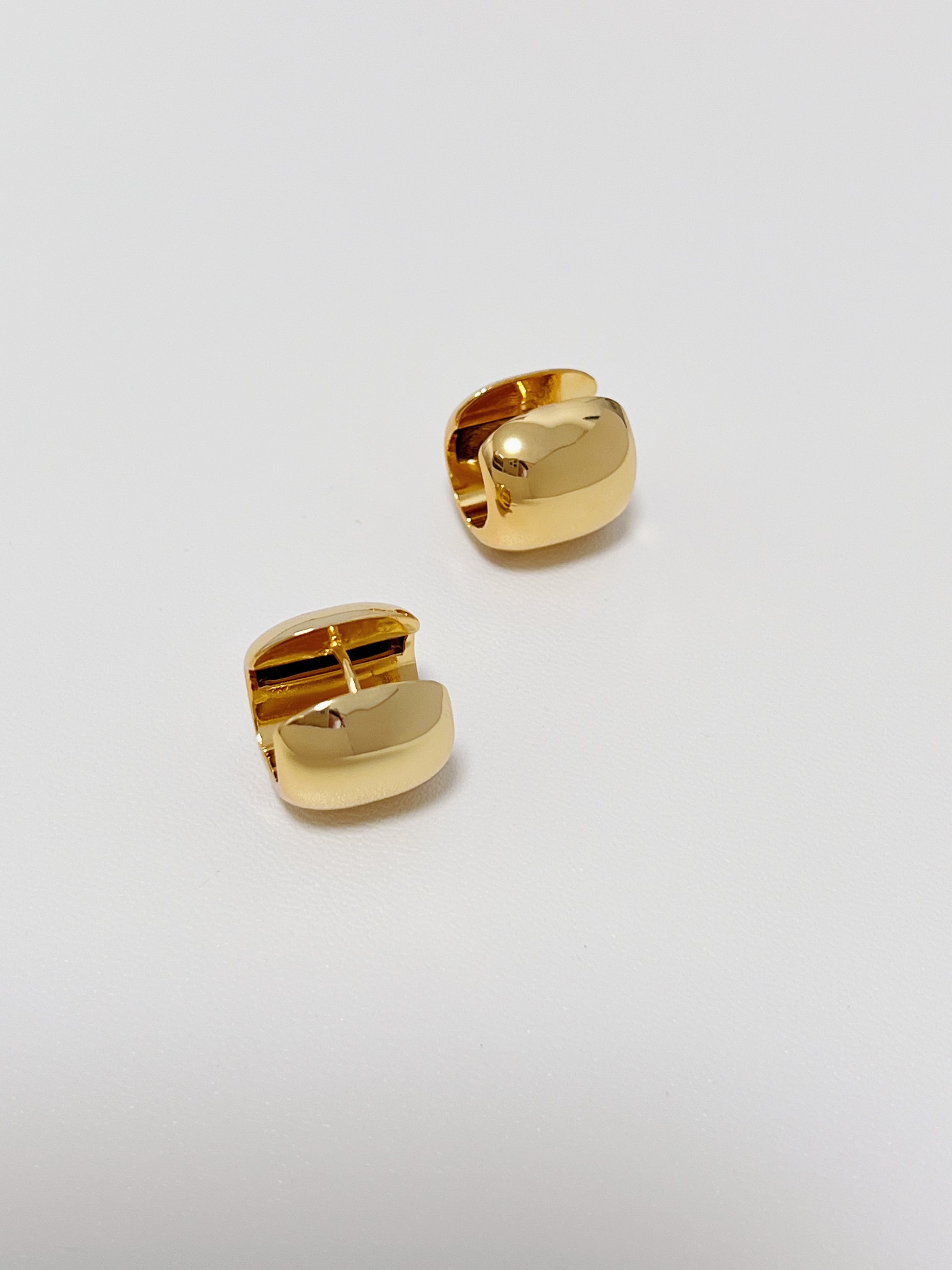 Two gold huggie hoops on a light gray background