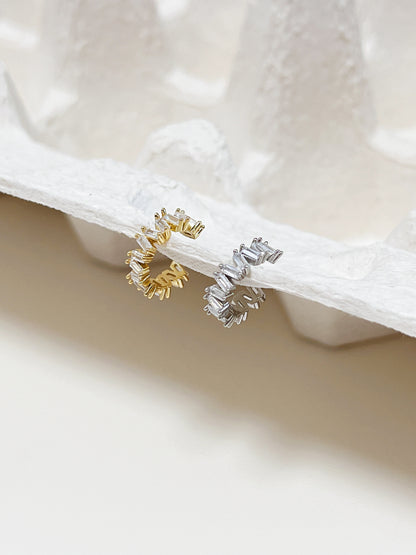 Gold and silver baguette cut diamond cuff earrings on a white surface with a textured background