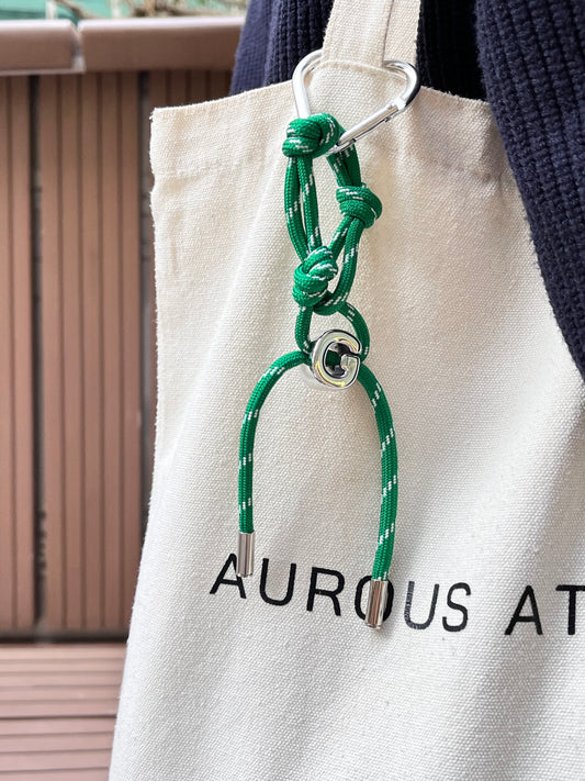 Model profile view showcasing a green personalized large letter G charm clipped onto a canvas tote bag