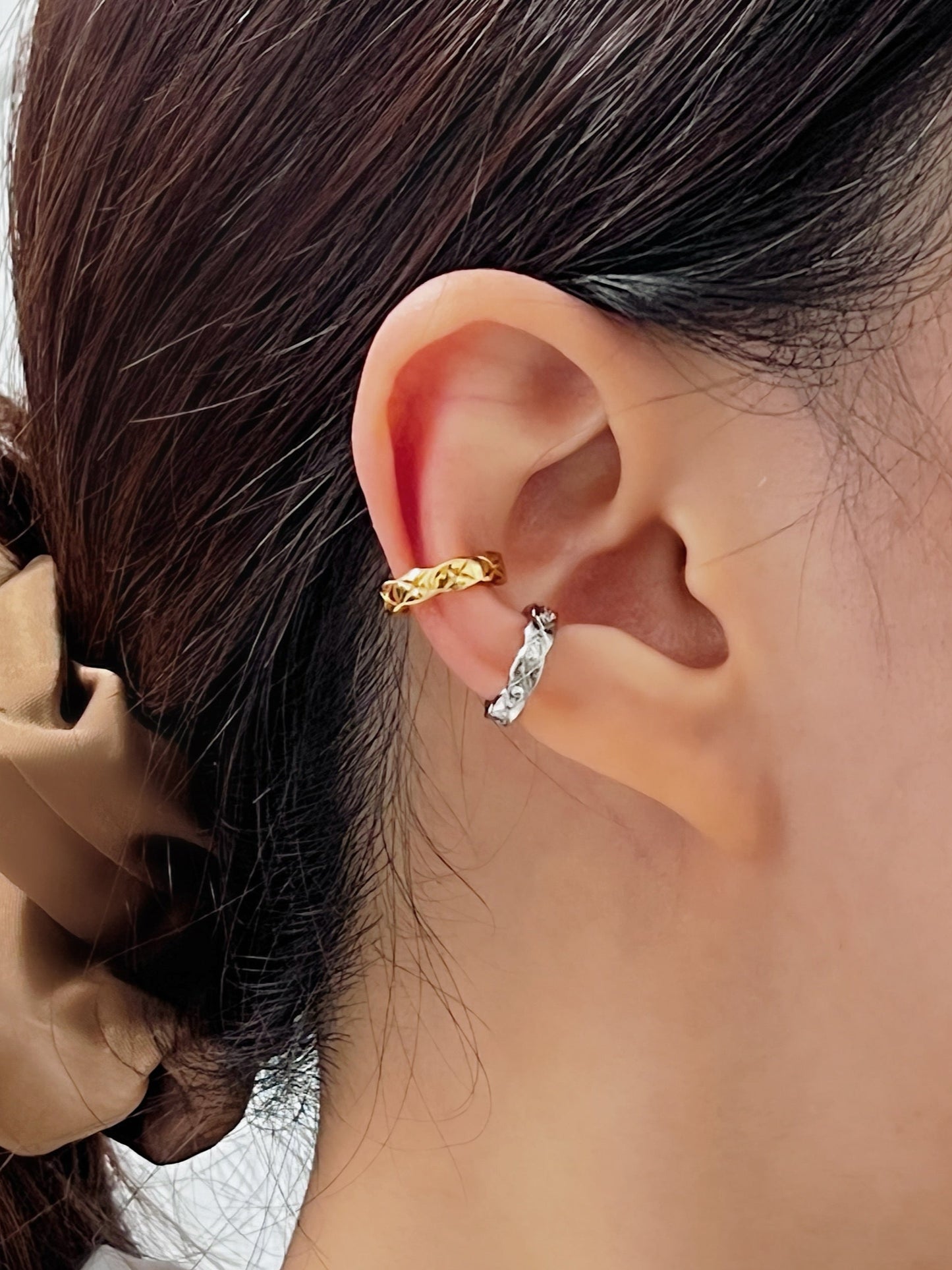 Close-up of a person wearing gold and silver ear cuffs with a blurred background.