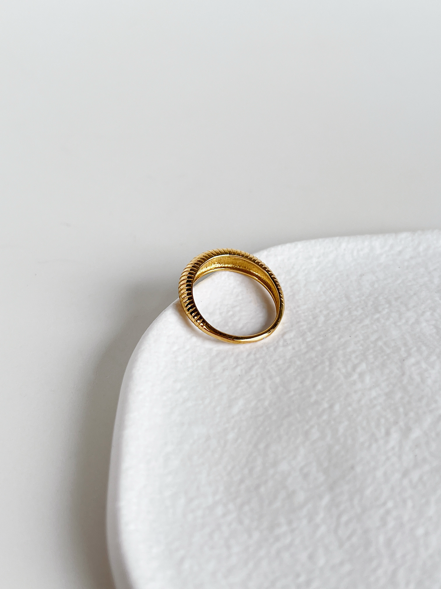 Gold dome ring on a white ceramic plate with a light gray background