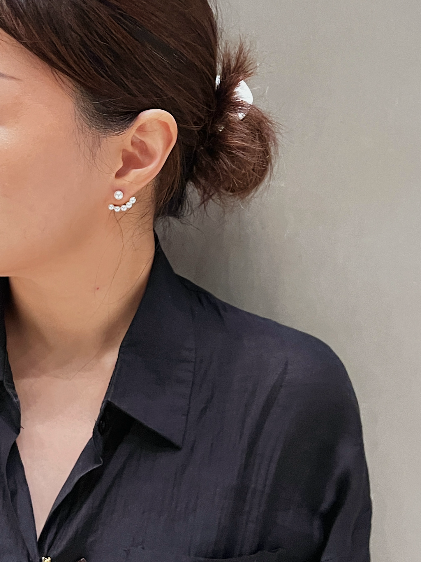 Close-up of a person wearing pearl ear jacket earrings with a neutral background