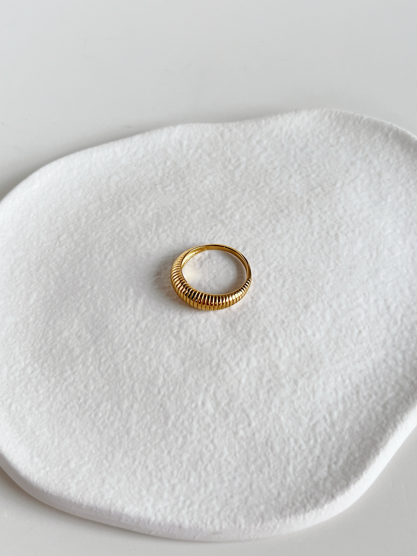 Gold ribbed dome ring on a textured white surface