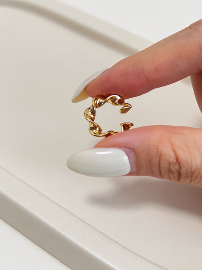 Gold twisted ear cuff earring design held by a hand with white nail polish on a light background