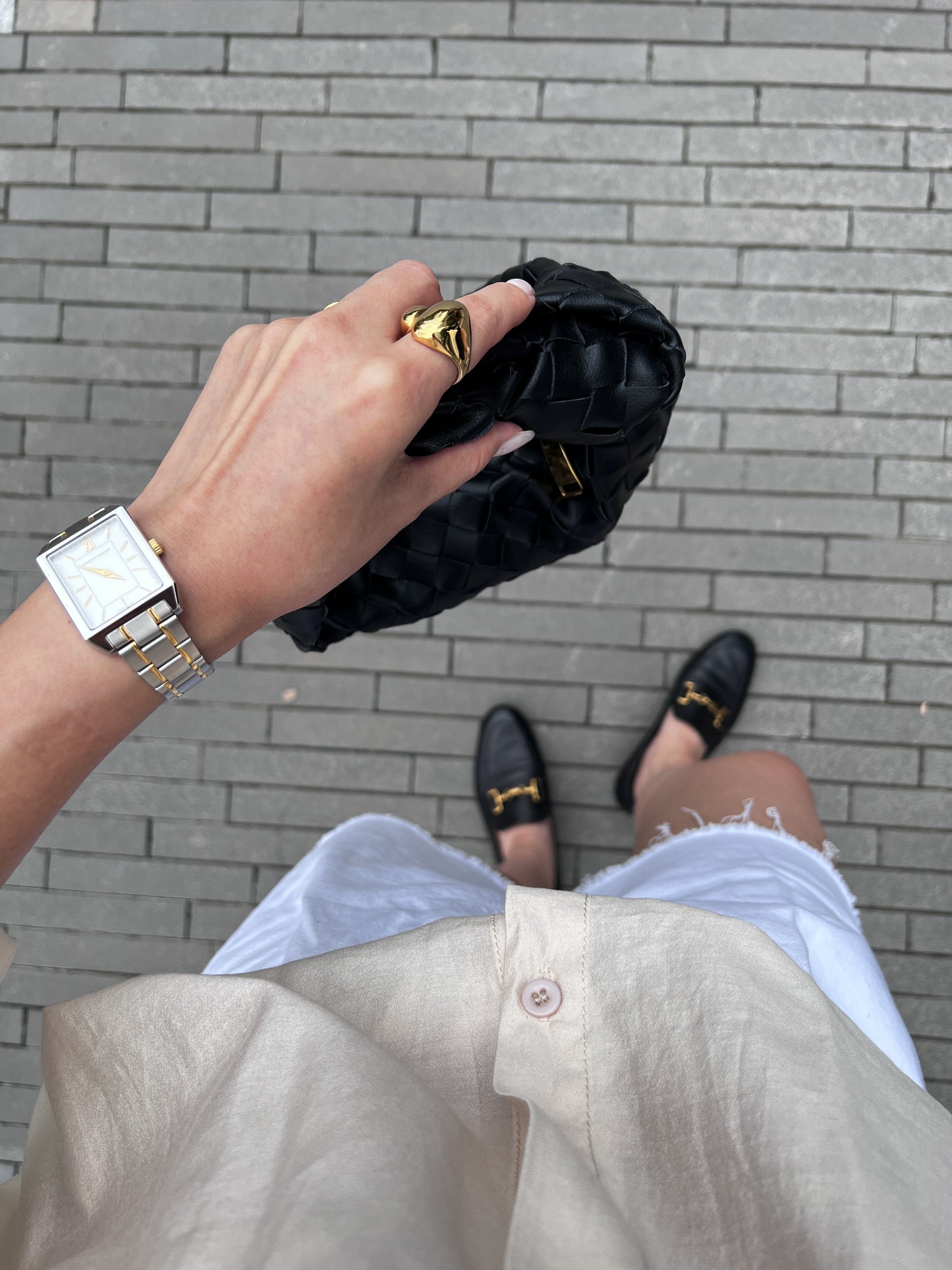 Person holding a black clutch with gold accents on a gray brick pavement.