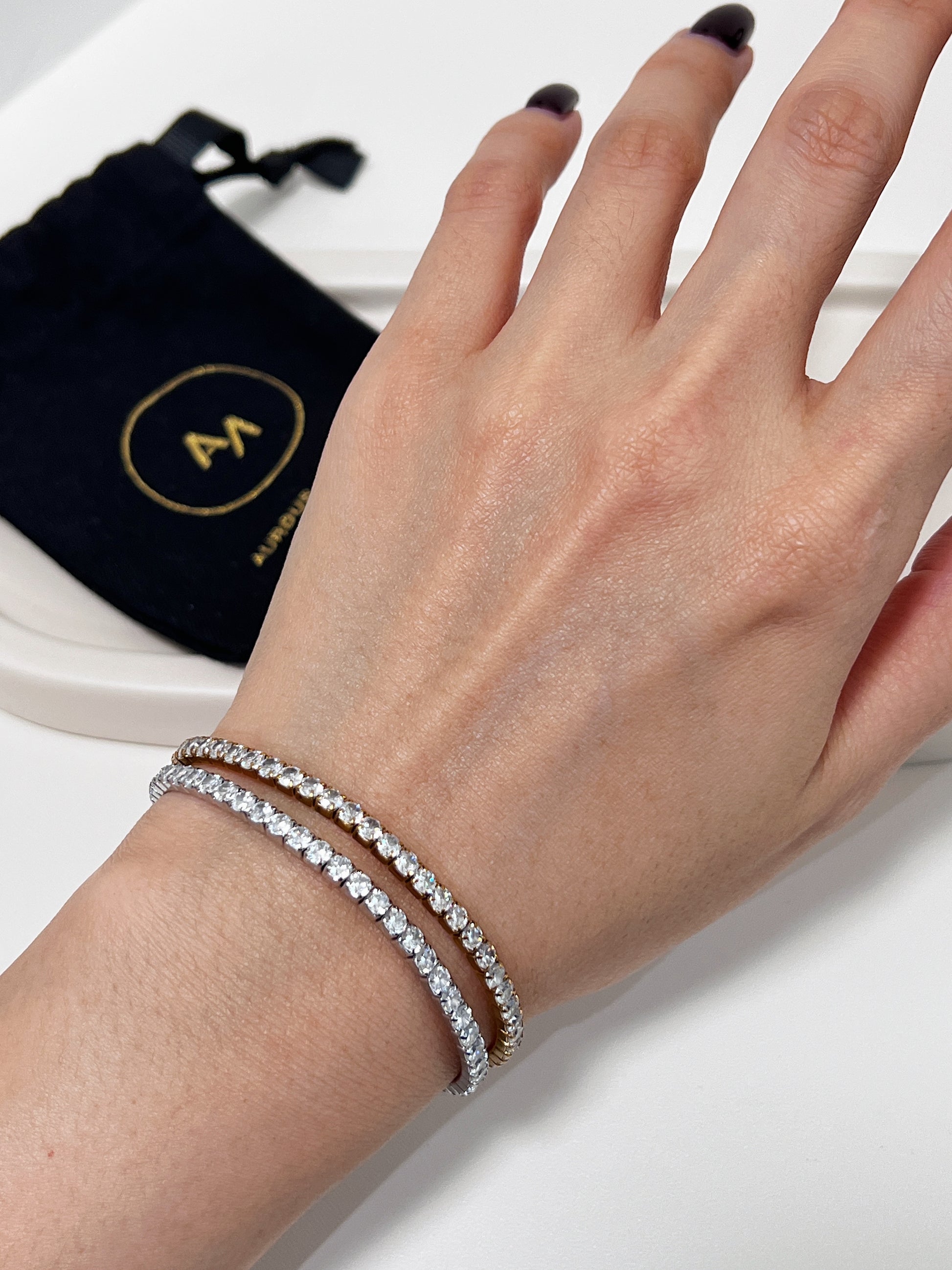 Hand wearing a silver diamond tennis bracelet with a black pouch in the background