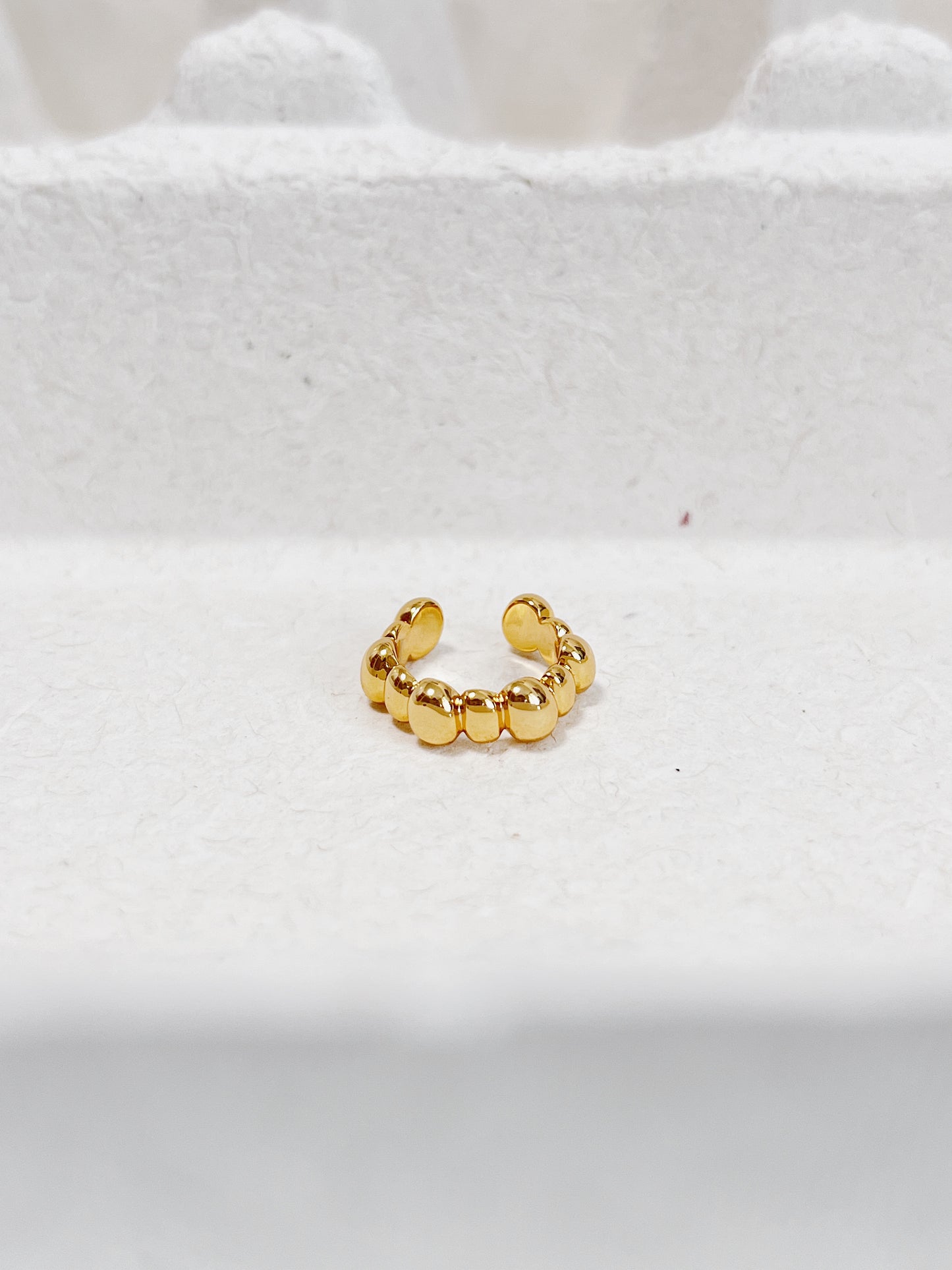 Gold beaded ear cuff on a white textured surface