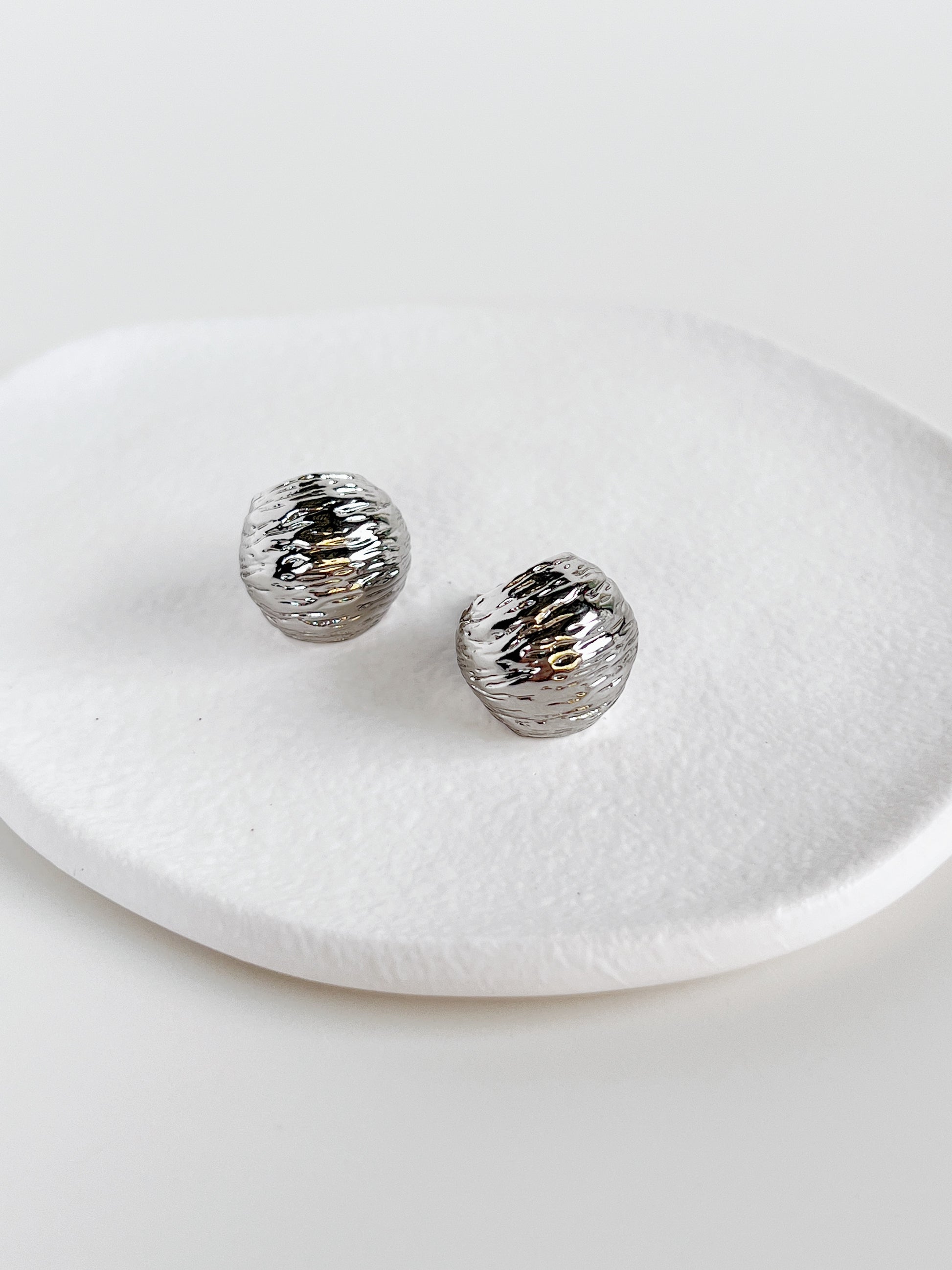 Silver textured round hoop earrings on a white dish