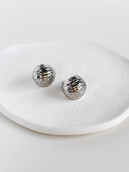 Silver textured round hoop earrings on a white dish