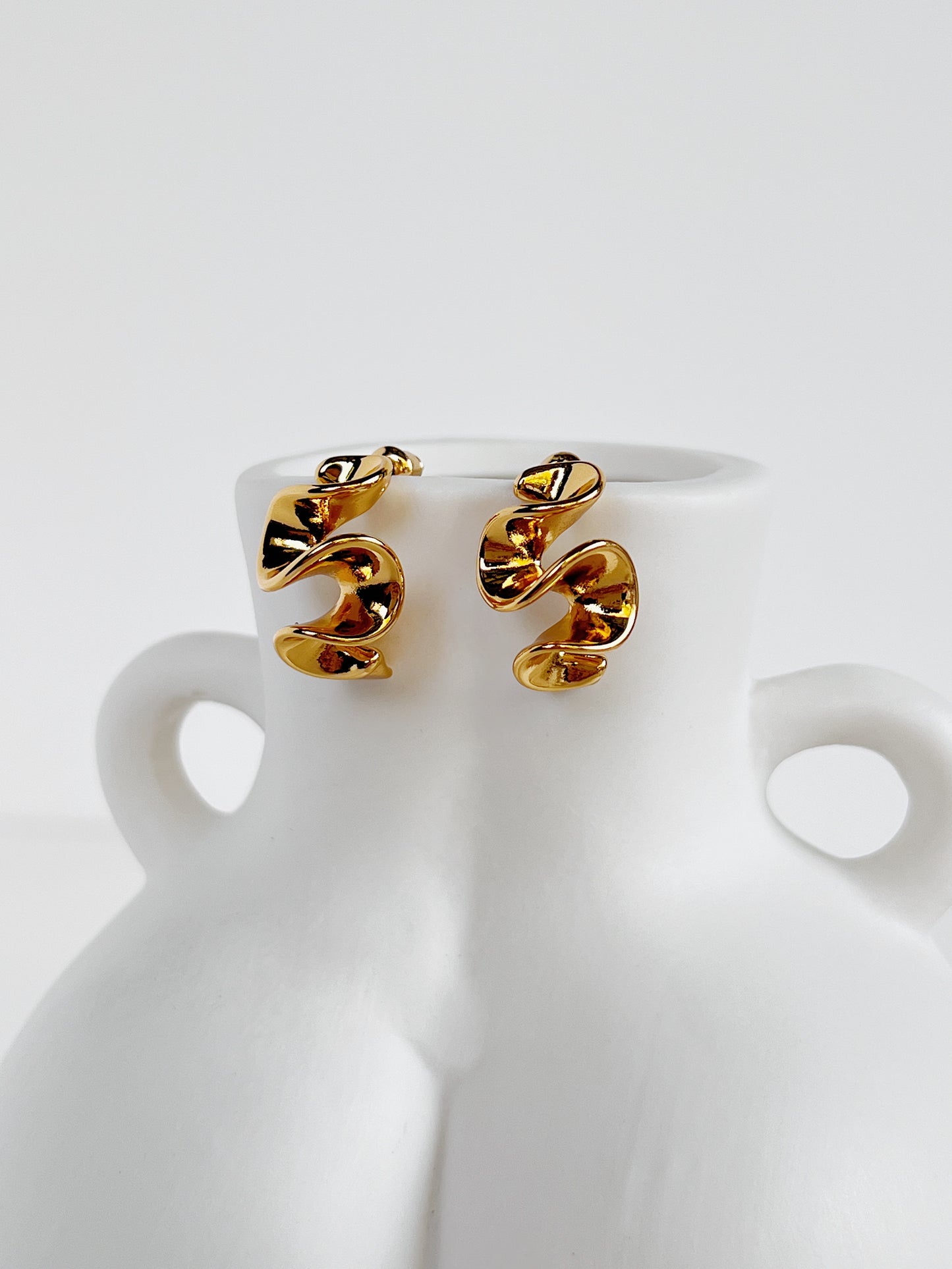 Gold spiral earrings on a white ceramic vase