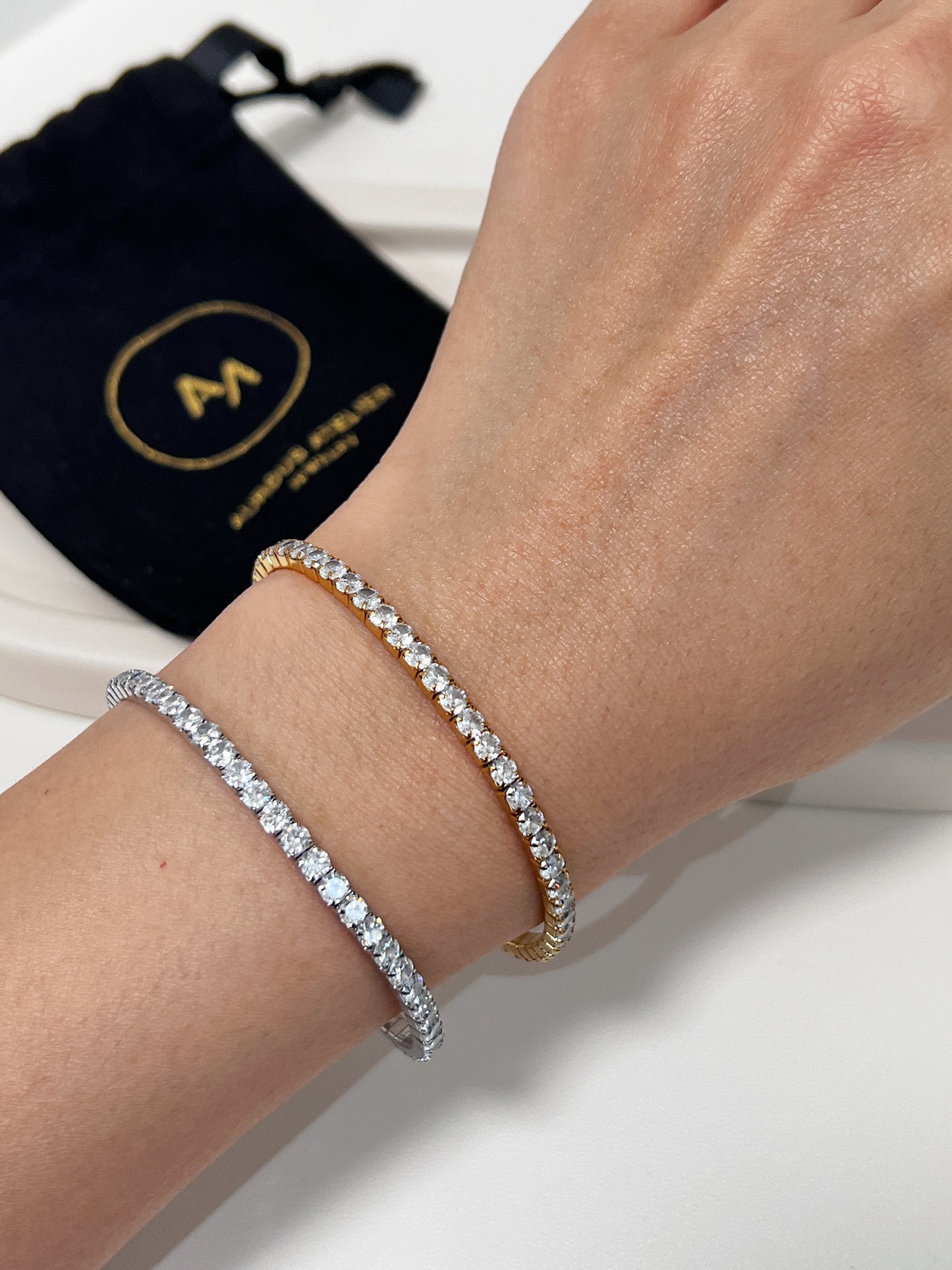 Silver and gold tennis bracelet on a wrist with a black drawstring bag in the background