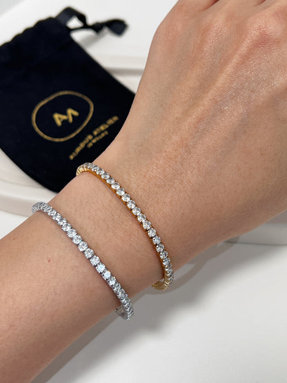Silver and gold tennis bracelet on a wrist with a black drawstring bag in the background