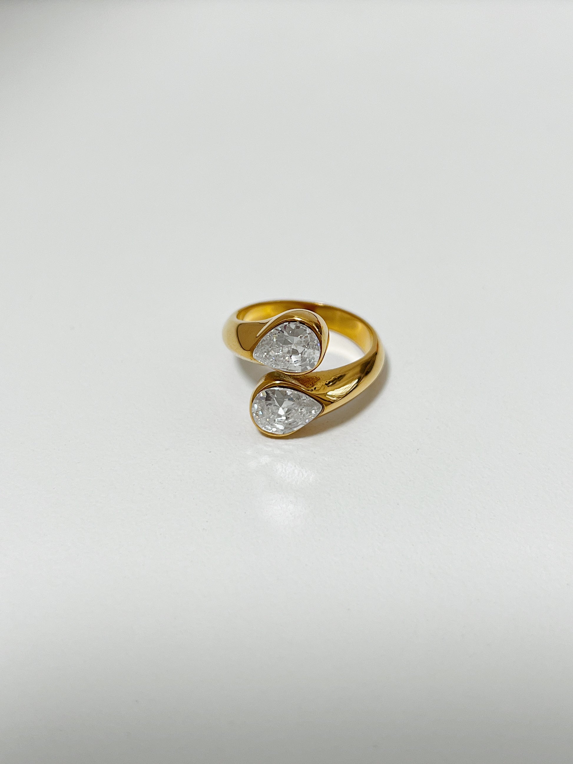 Gold ring with two clear gemstones on a light gray background