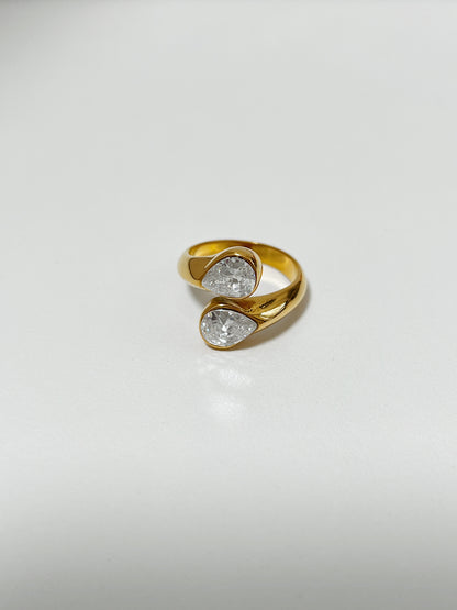 Gold ring with two clear gemstones on a light gray background