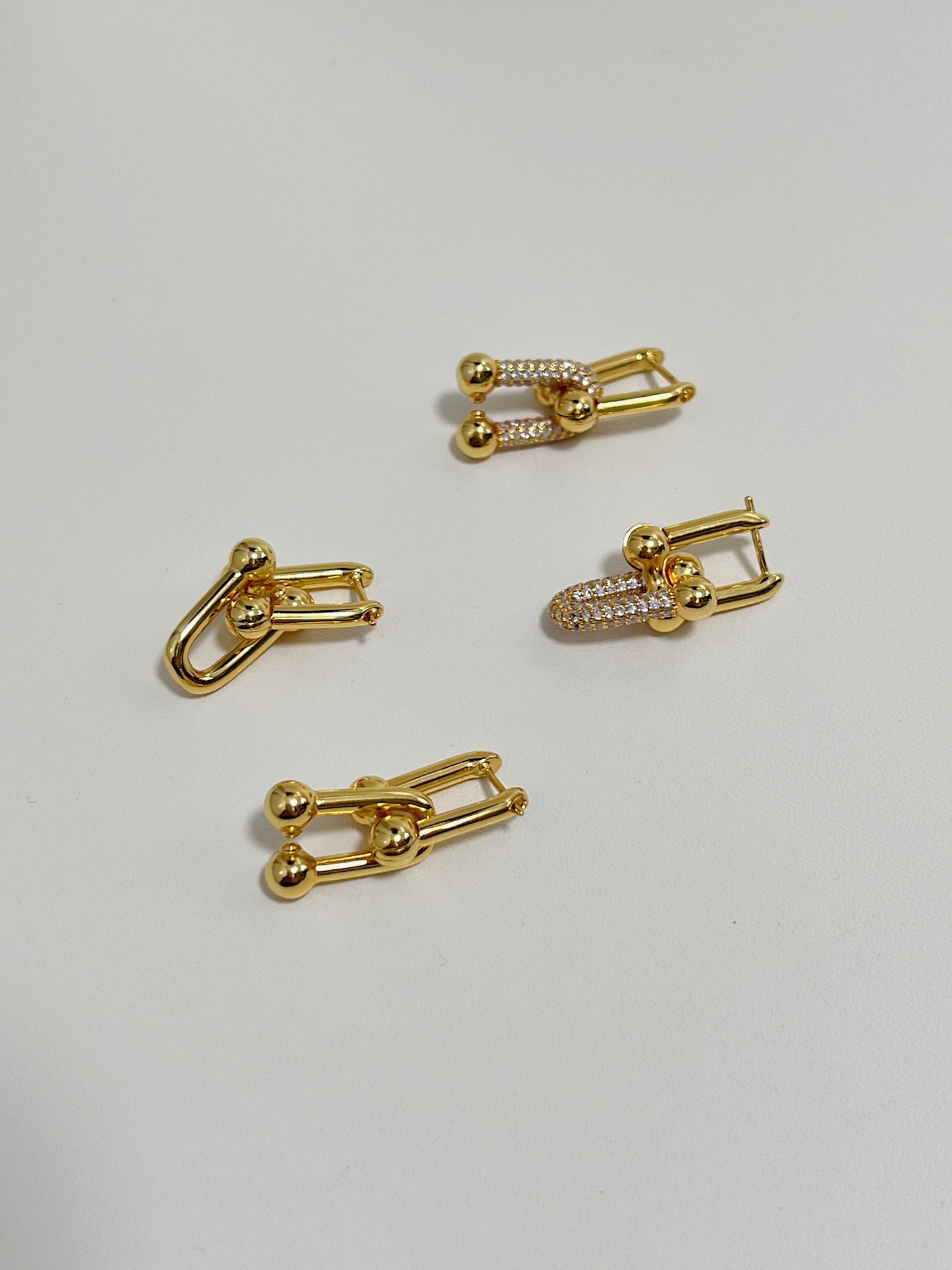 Close-up of the 2 pairs of gold link earrings with and without diamonds display on a white surface. 