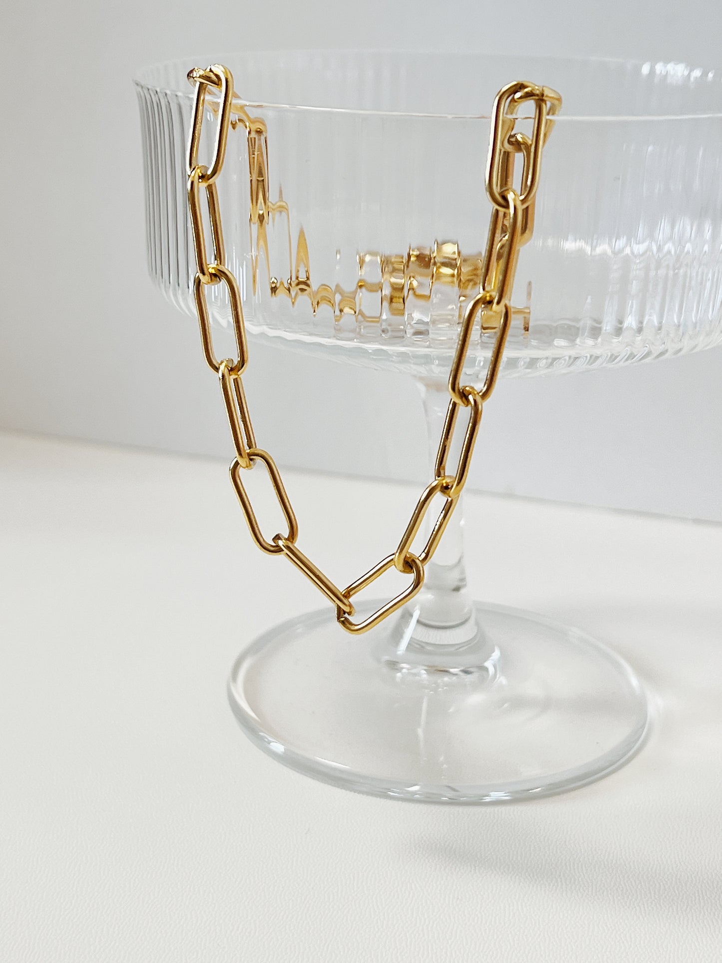 Gold chain necklace on a clear cocktail glass with a white background