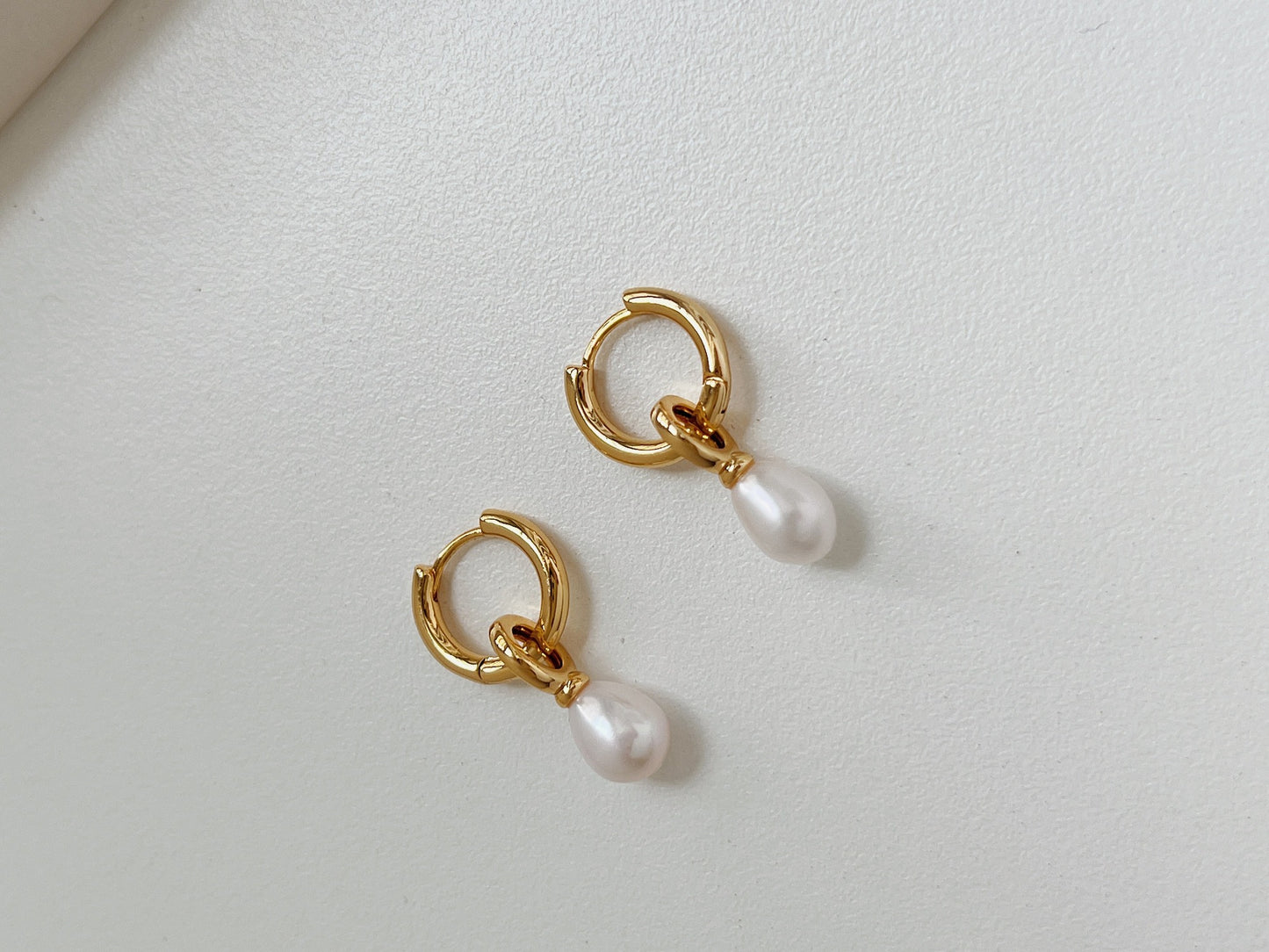 A pair of gold dangle pearl earrings flatlay on a white background.