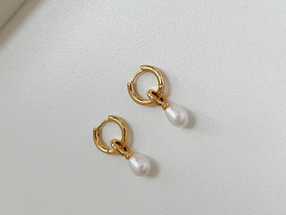 A pair of gold dangle pearl earrings flatlay on a white background.