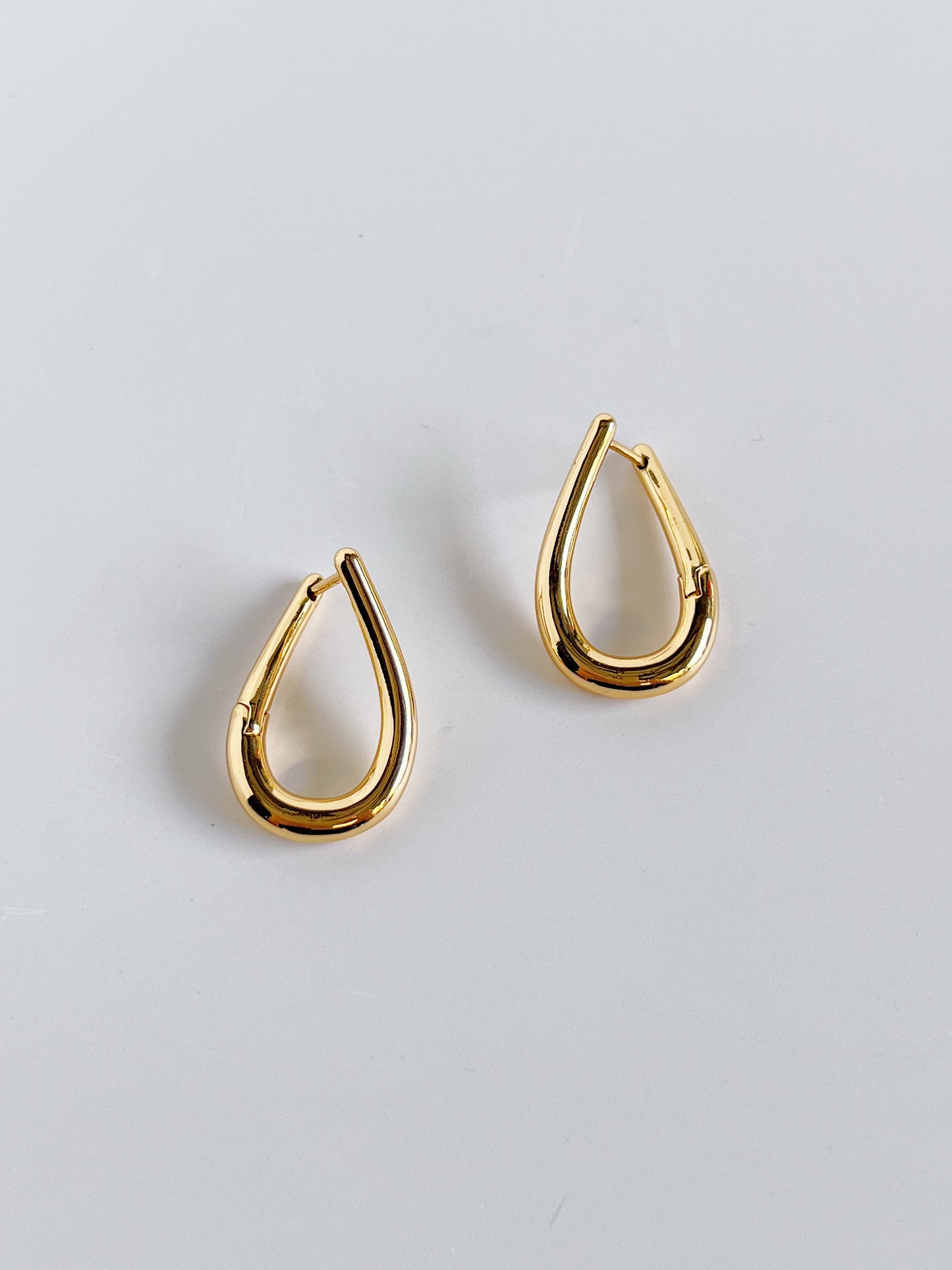 Gold twill hoop earrings on a light gray background