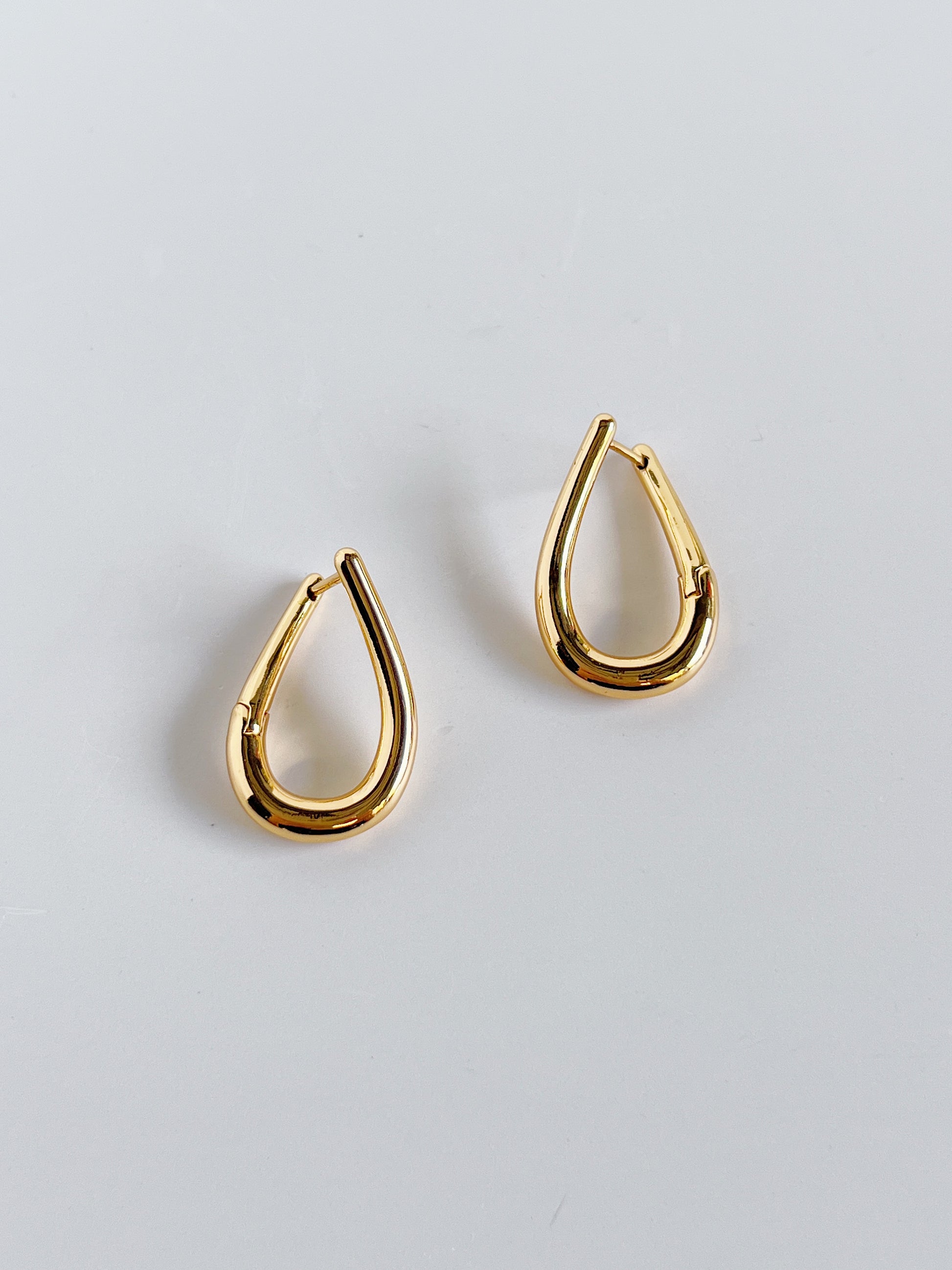 Gold twill hoop earrings on a light gray background
