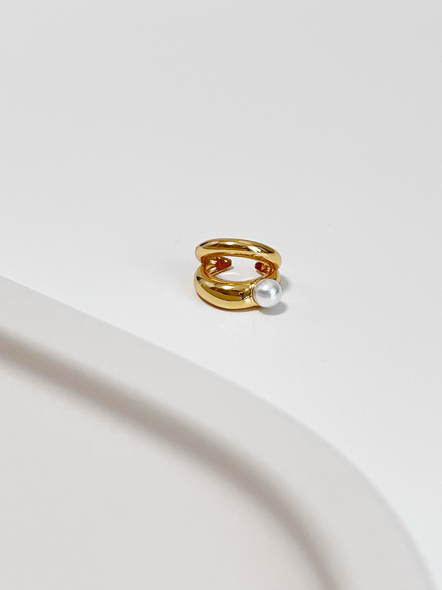 Gold ear cuff with a pearl on a light background