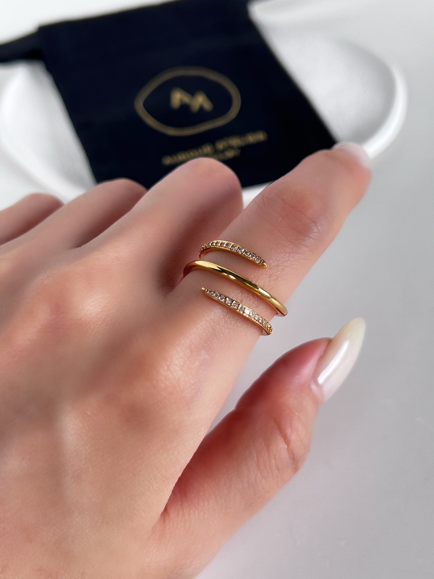 Gold spiral ring on a finger with aurous atelier brand logo in the background
