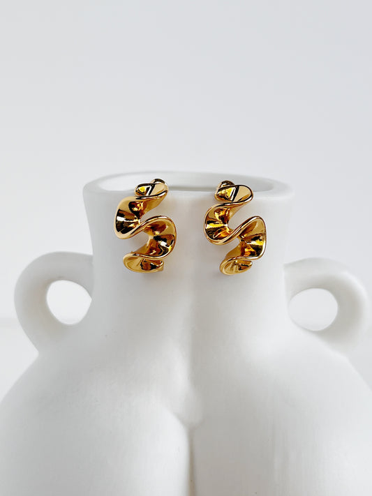 Gold spiral earrings on a white ceramic vase