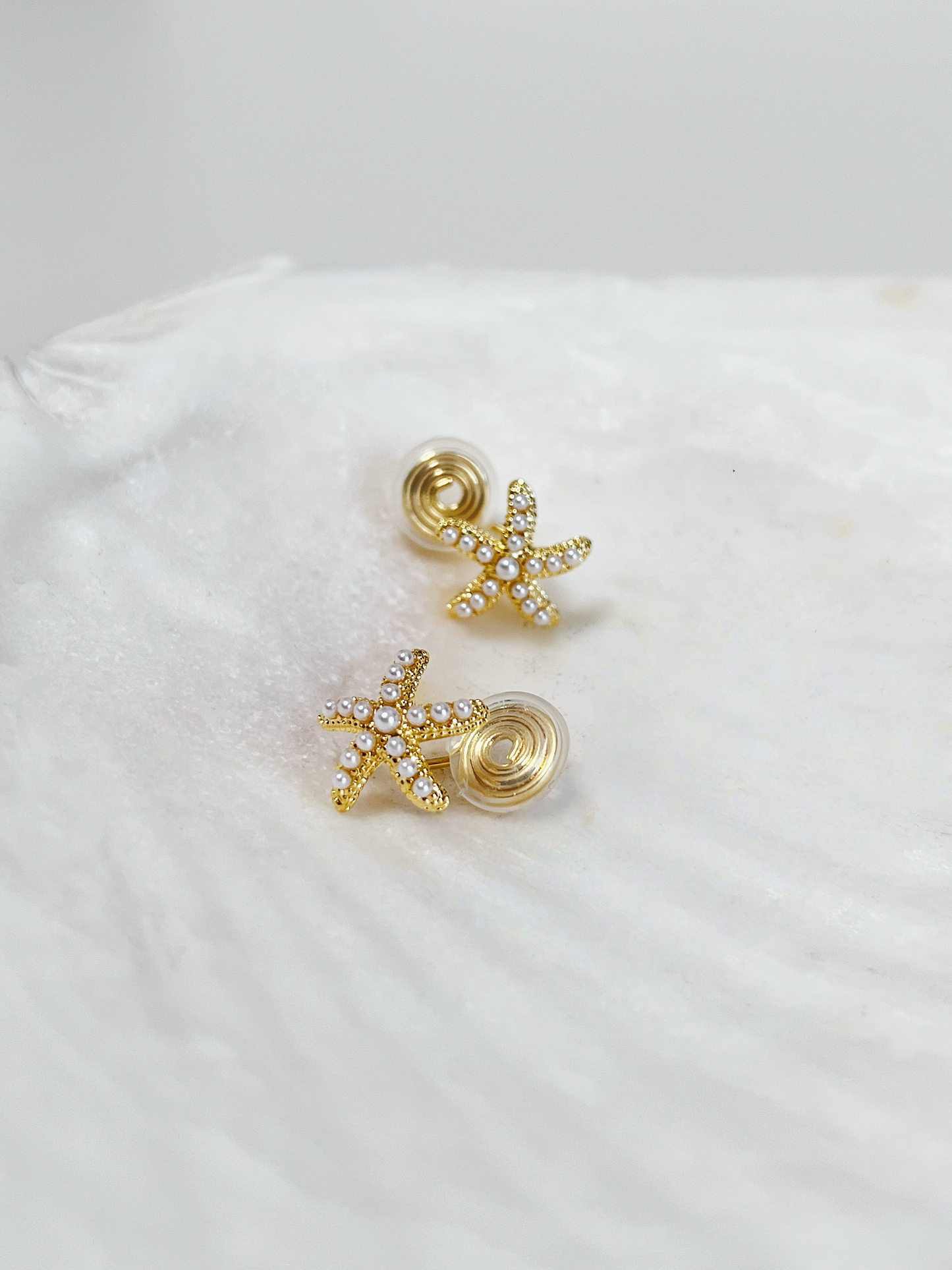 Gold starfish earrings on a white shell