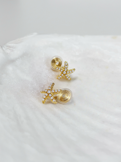 Gold starfish earrings on a white shell
