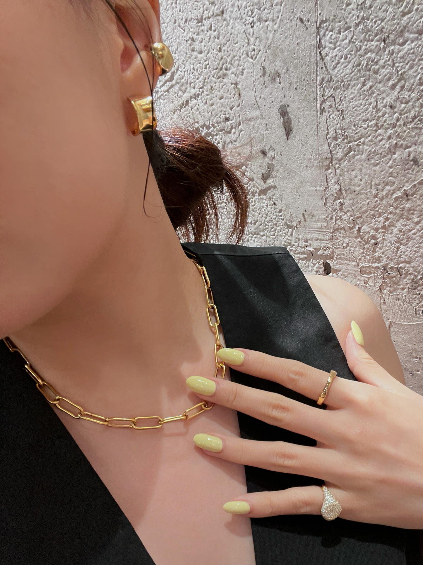 Close-up of a person wearing gold jewelry including earrings, necklace, and ring.