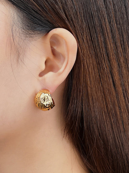 Gold textured earring worn by a person with long brown hair on a neutral background