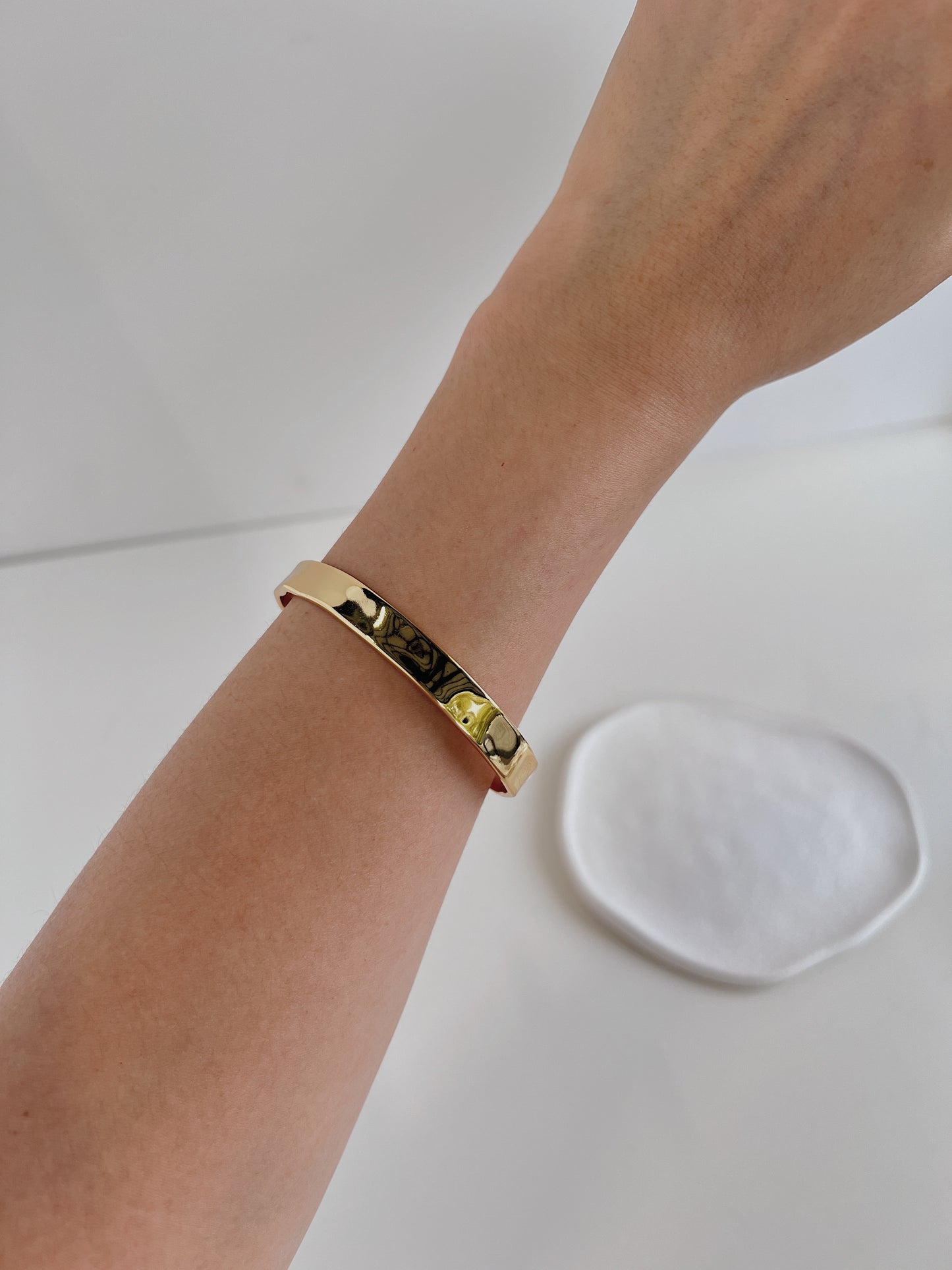 A woman wearing a minimalist gold-tone cuff bangle, a simple yet striking accessory.