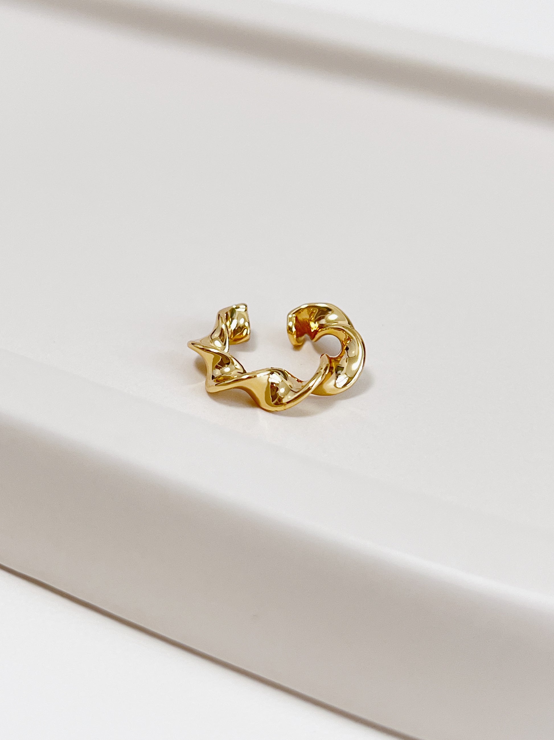 Gold twist ear cuff on a light beige surface
