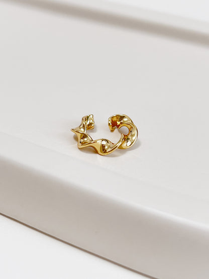 Gold twist ear cuff on a light beige surface