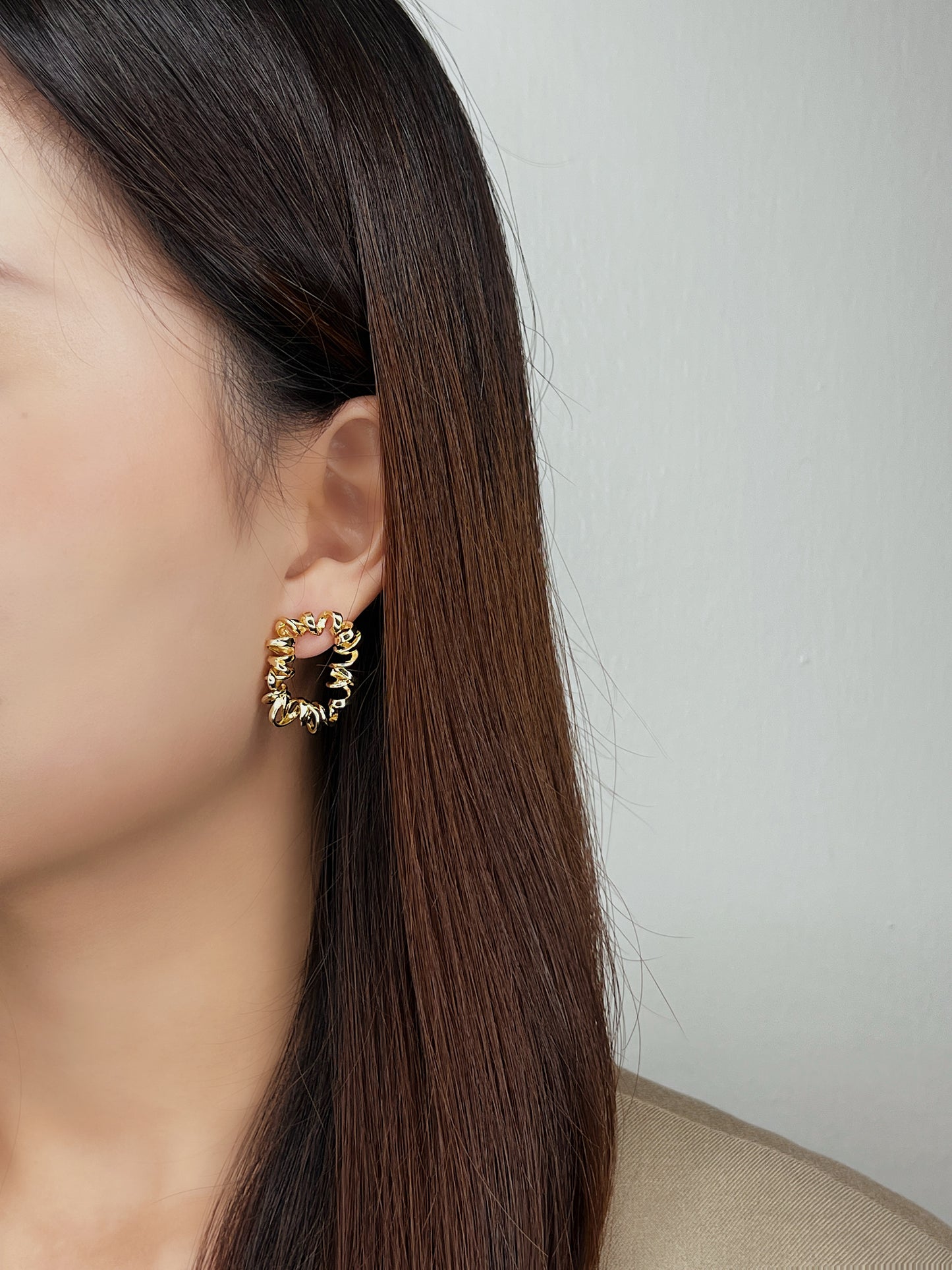 Close-up of a person wearing gold wire curly hoop earrings with a plain background