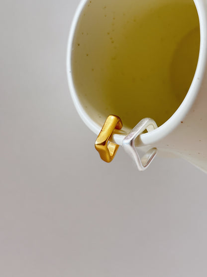 Gold and silver square shape ear cuff on a ceramic cup against a light gray background
