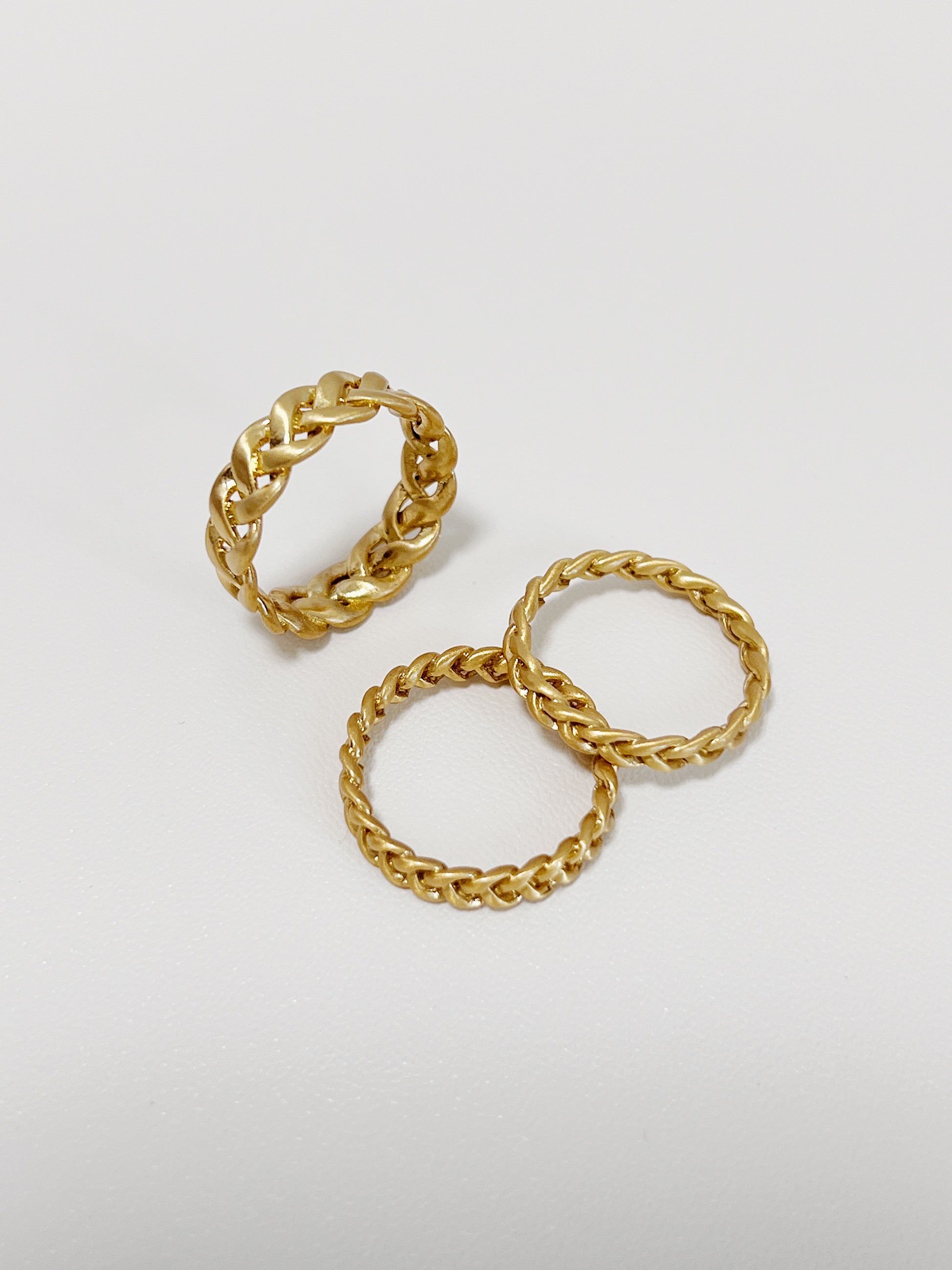 Three gold braided-style rings on a light gray background