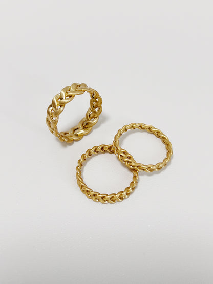 Three gold braided-style rings on a light gray background