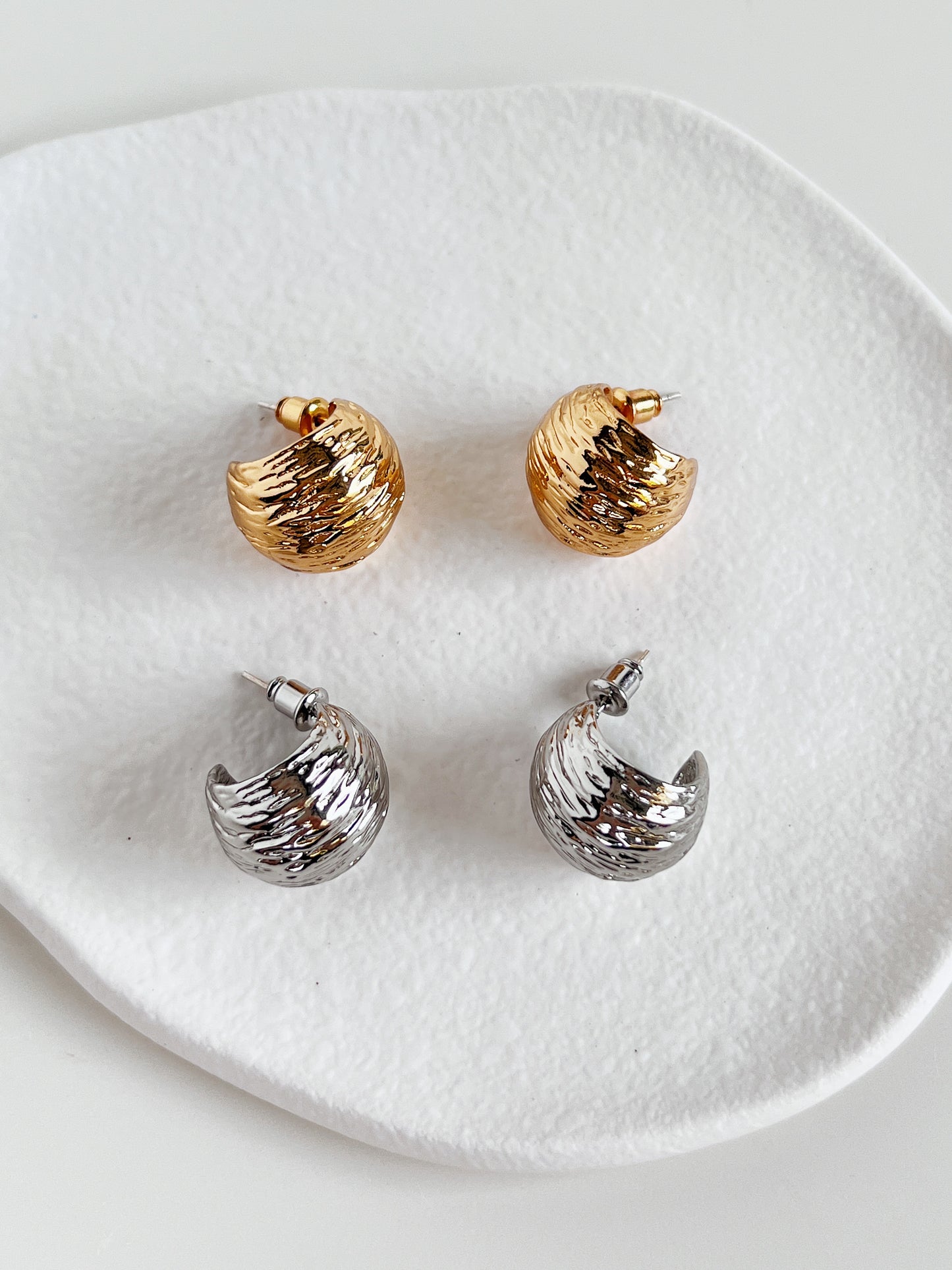 Pair of gold and silver earrings on a white ceramic dish