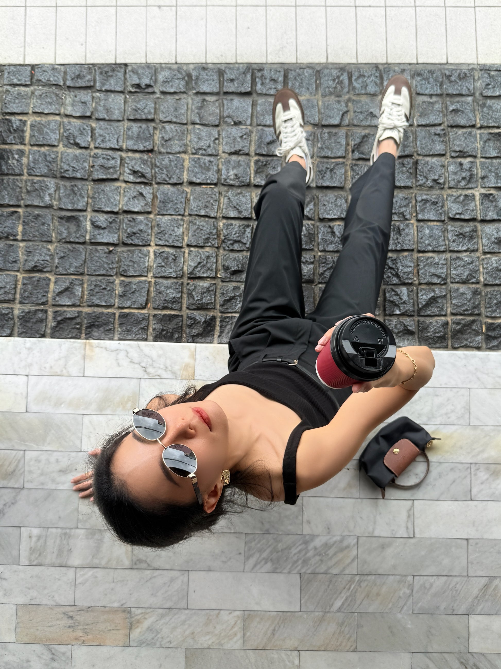 Person sitting on a stone pavement holding a red cup