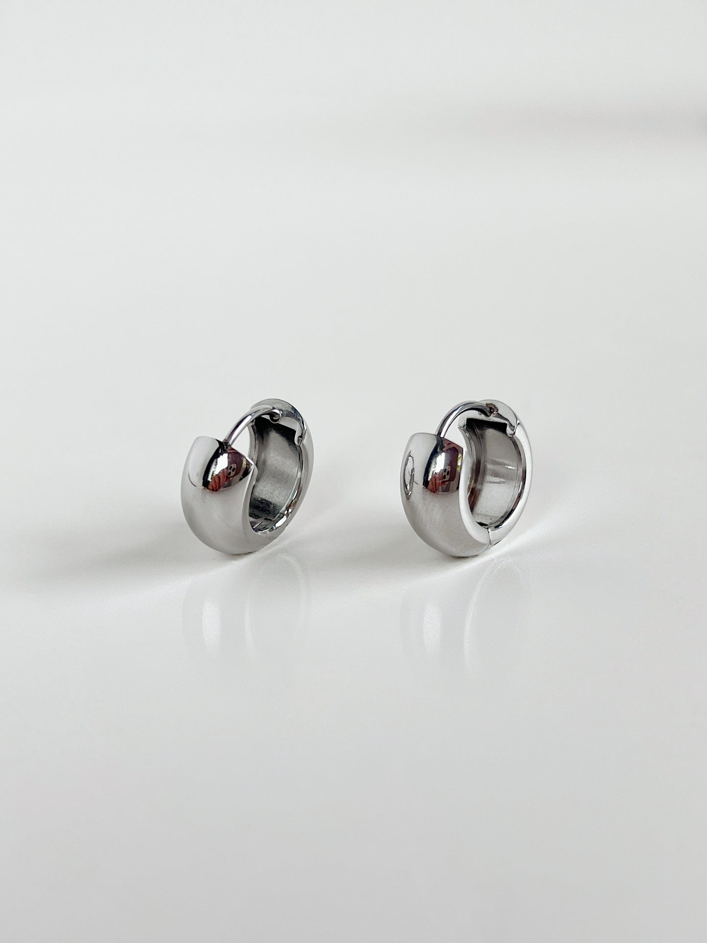 Close-up of Amie Chunky Huggie Hoops in silver on white background.