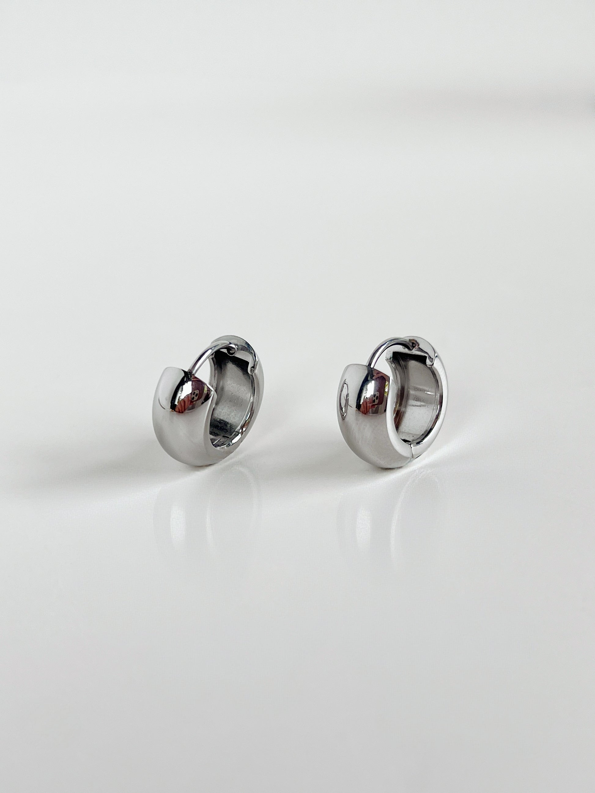 Close-up of Amie Chunky Huggie Hoops in silver on white background.