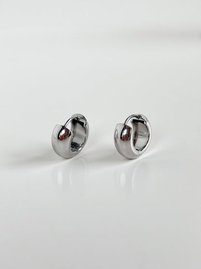 Close-up of Amie Chunky Huggie Hoops in silver on white background.